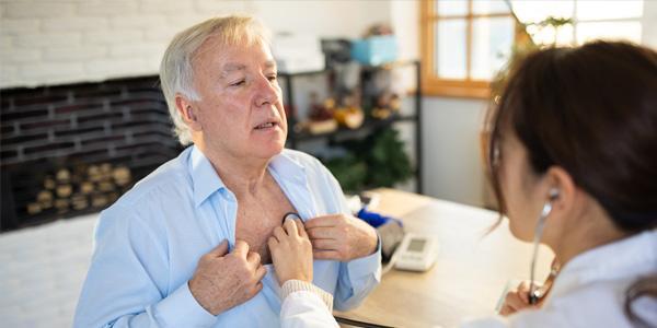 Eine Kardiologin untersucht einen älteren Patienten mit chronischer Herzinsuffizienz.