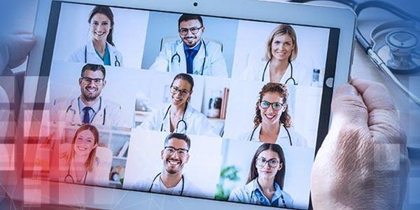 Tablet Close mit Kachelbildern von 9 Ärzten in den Händen eines Arztes, danebenliegendes Stethoskop Alternative: kleiner Haufen verschiedener loser Tabletten auf einem Beipackzettel